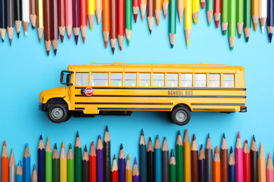 Photo of Flat lay composition with yellow school bus model on light blue background. Transport for students