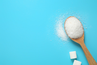 Photo of Sugar and spoon on light blue background, flat lay. Space for text