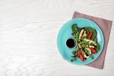 Plate with vegetable salad and balsamic vinegar on white wooden table, top view. Space for text