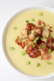 Tasty potato soup with bacon, green onion and croutons in bowl on white table, top view