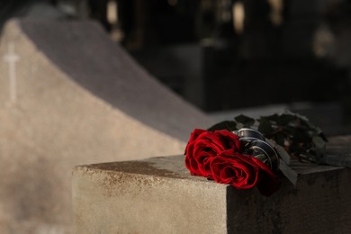 Photo of Red roses on grey tombstone outdoors, space for text. Funeral ceremony