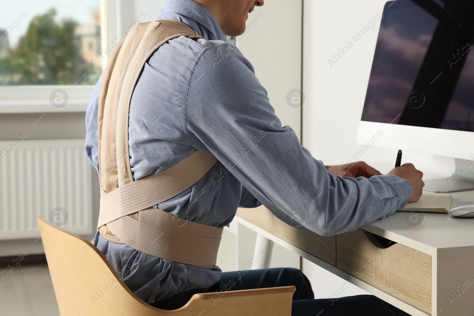 Photo of Closeup view of man with orthopedic corset working on computer in room