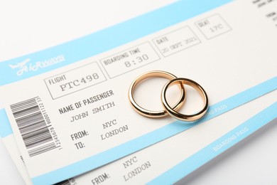 Honeymoon concept. Plane tickets and two golden rings on white background, closeup