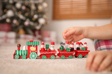 Photo of Little girl playing with colorful train toy in room decorated for Christmas, closeup