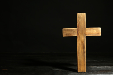 Christian cross on wooden table against black background, space for text. Religion concept