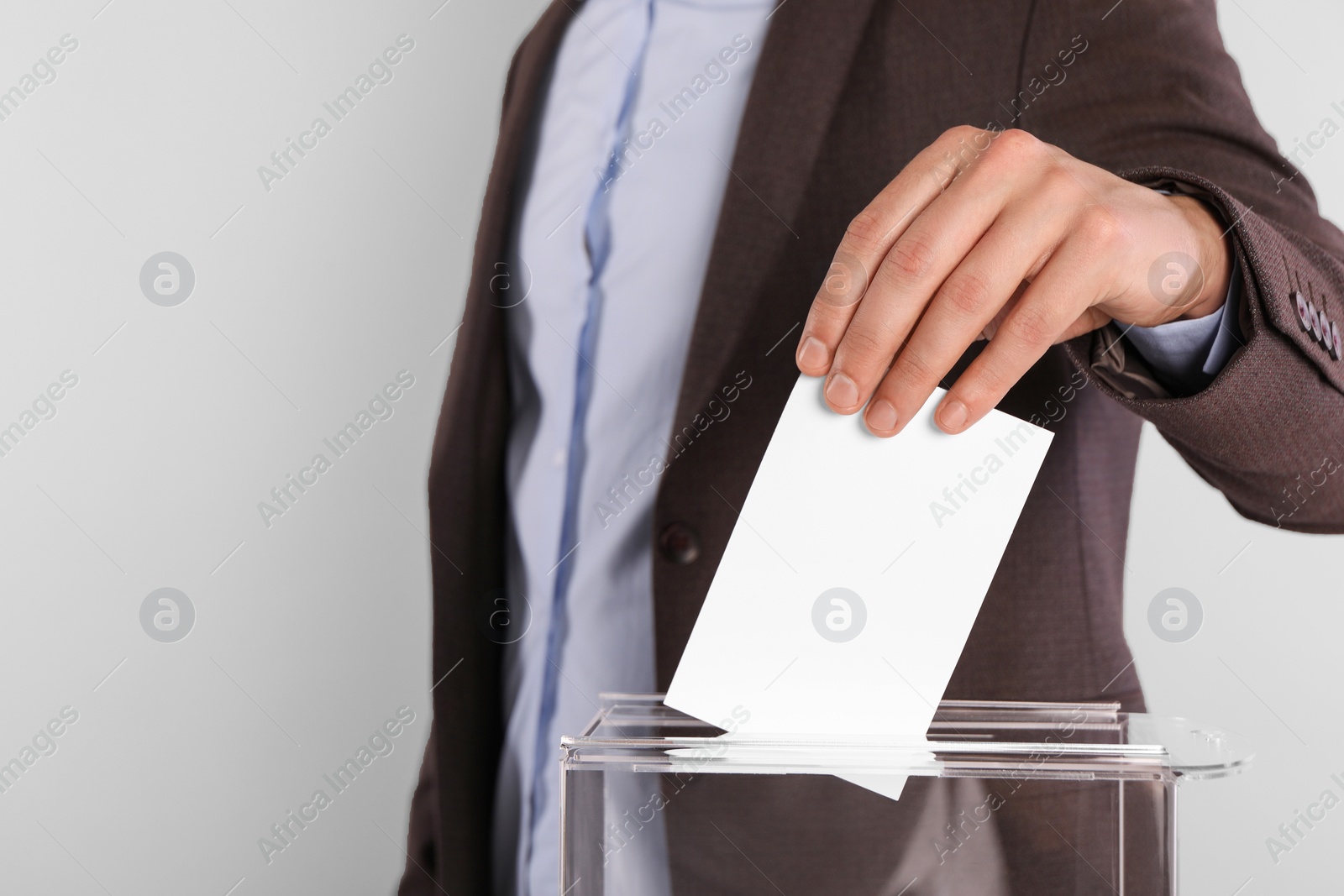 Photo of Man putting his vote into ballot box on light grey background, closeup. Space for text