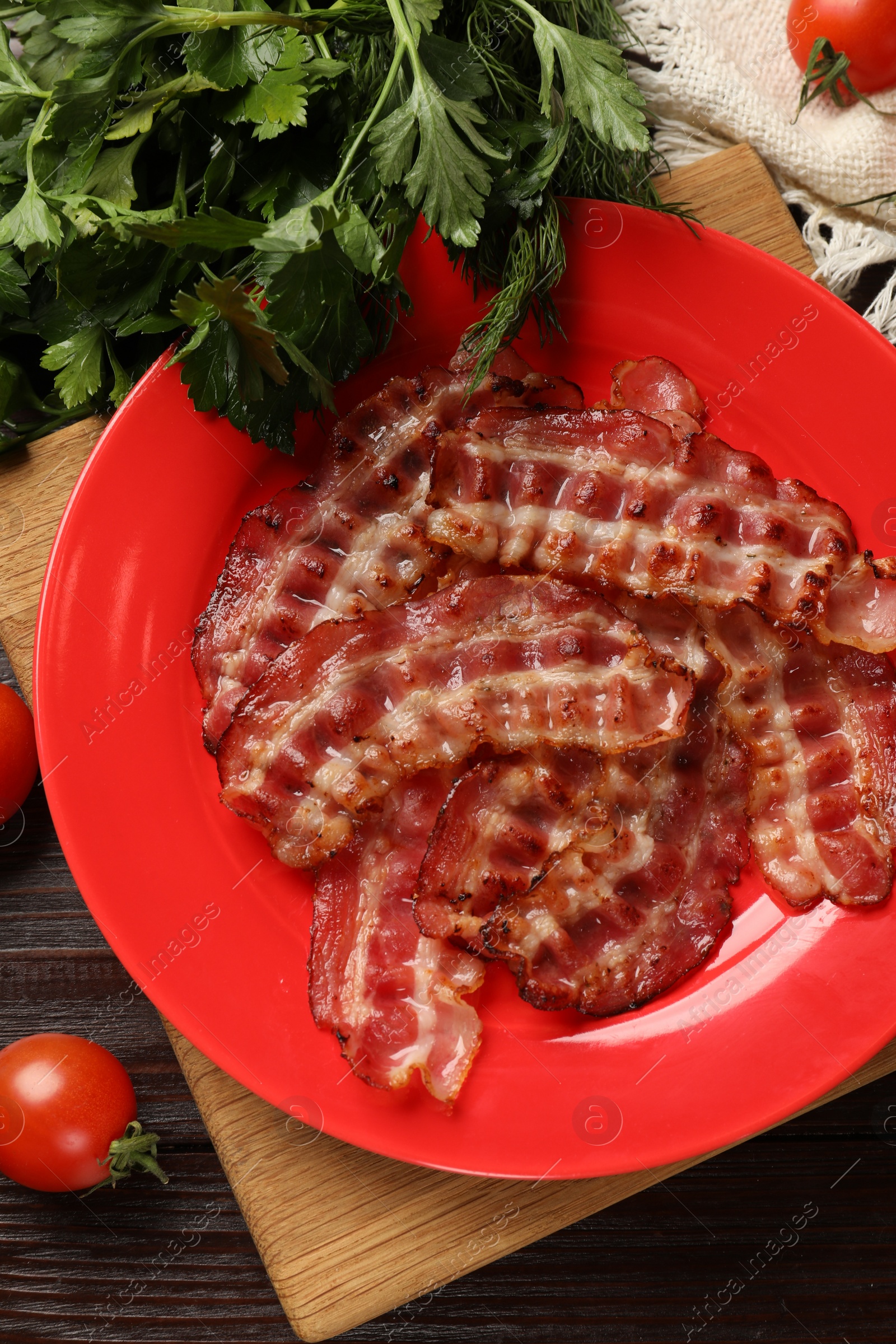 Photo of Plate with fried bacon slices, tomatoes and parsley on wooden table, flat lay