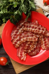 Plate with fried bacon slices, tomatoes and parsley on wooden table, flat lay