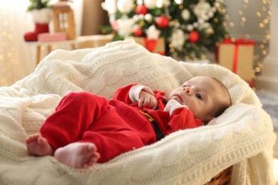 Photo of Cute little baby on knitted blanket in room decorated for Christmas