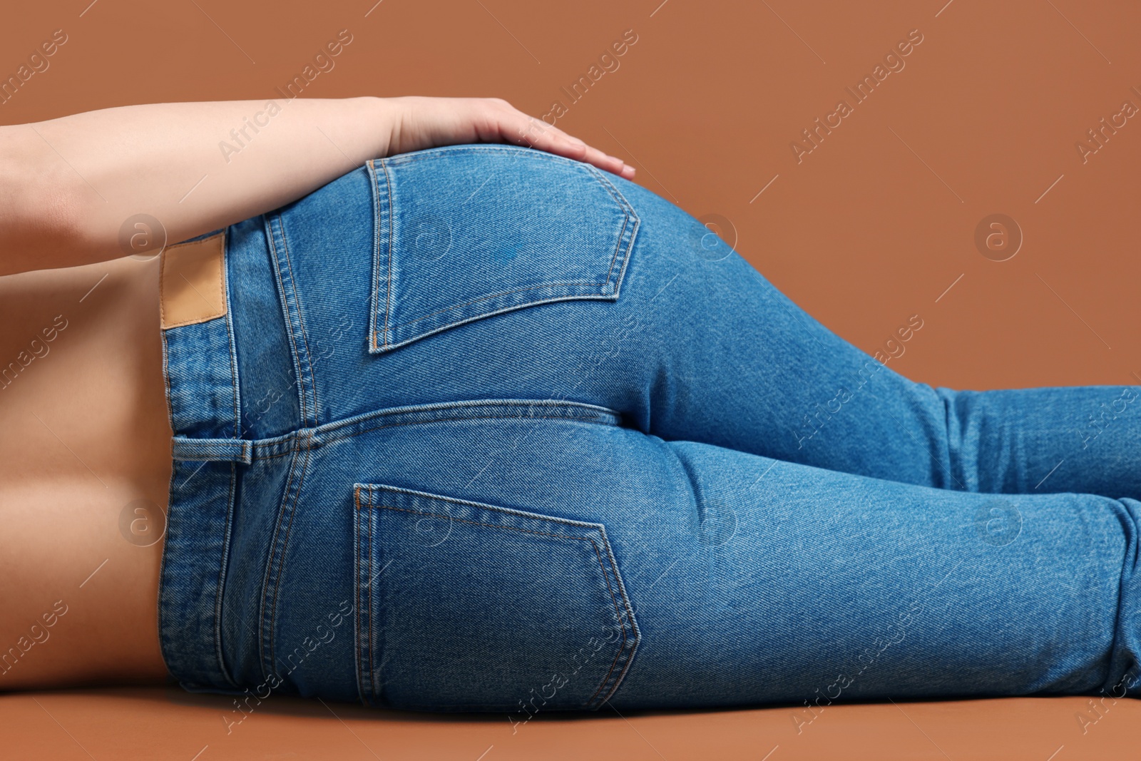 Photo of Woman in stylish jeans on brown background, closeup