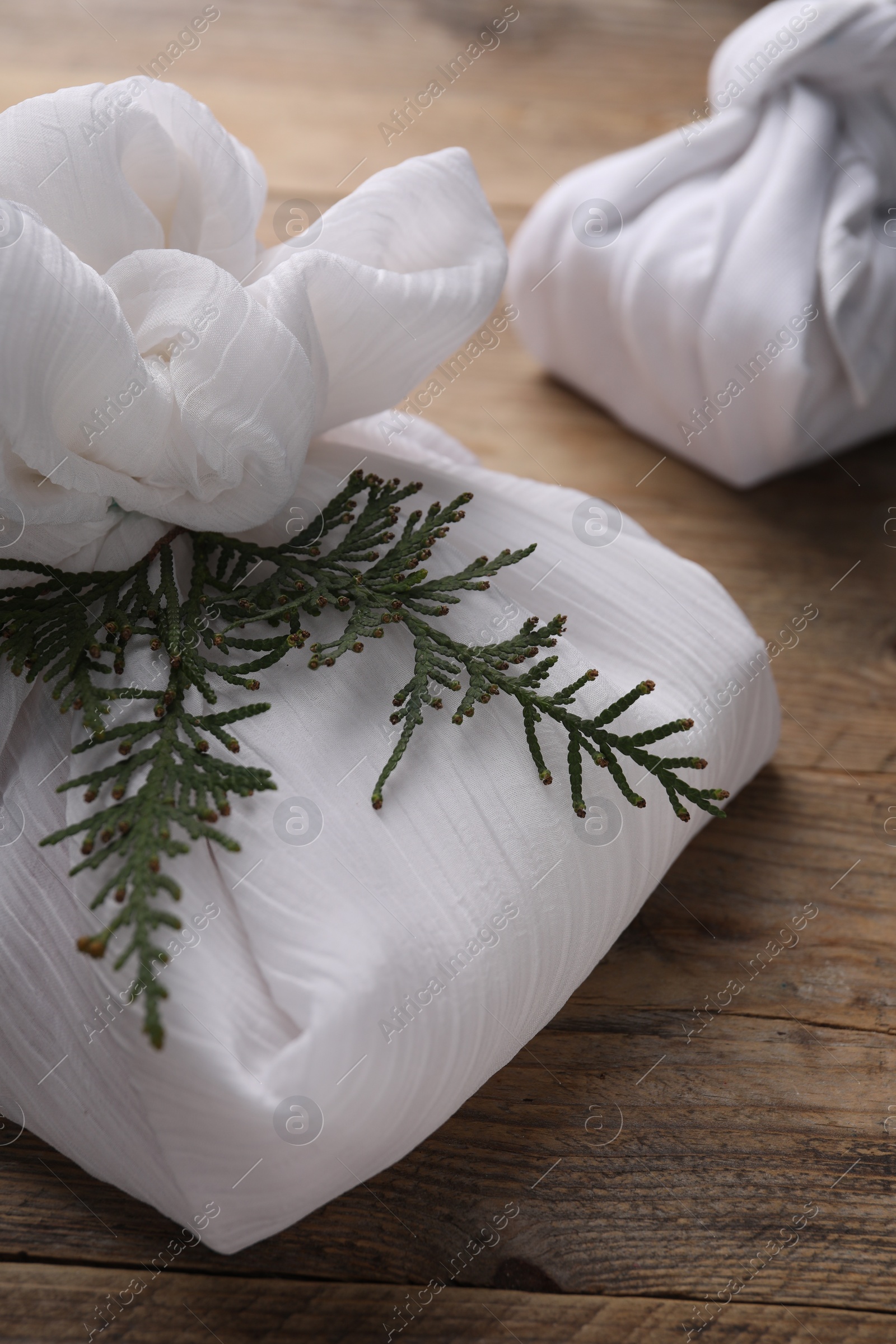 Photo of Furoshiki technique. Gifts packed in white fabric and thuja branches on wooden table