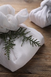 Photo of Furoshiki technique. Gifts packed in white fabric and thuja branches on wooden table