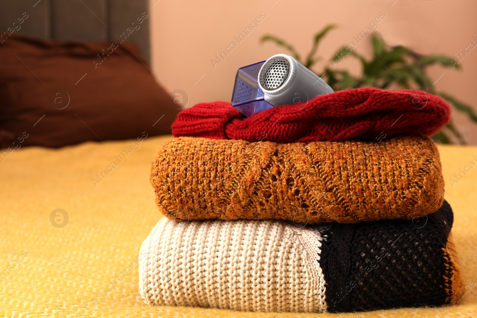 Photo of Modern fabric shaver and knitted clothes on bed indoors, closeup. Space for text