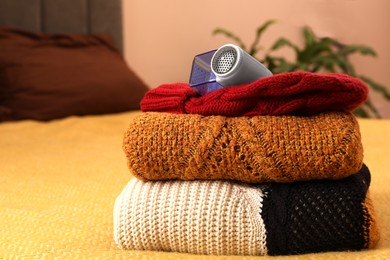 Photo of Modern fabric shaver and knitted clothes on bed indoors, closeup. Space for text