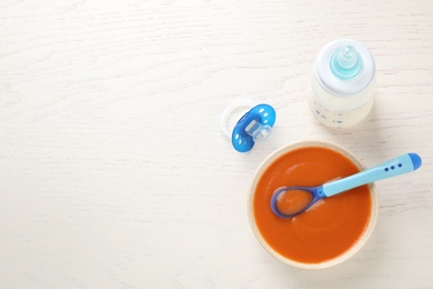 Photo of Bowl of healthy baby food, pacifier and bottle with milk on white wooden table, flat lay. Space for text