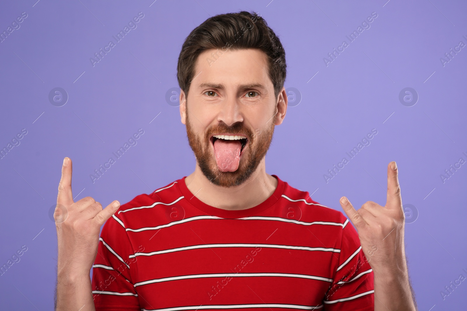 Photo of Man showing his tongue and rock gesture on violet background