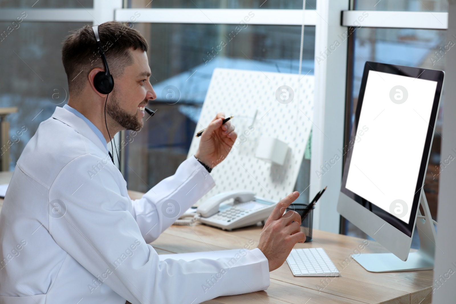 Photo of Doctor with headset consulting patient online at desk in clinic, space for text. Health service hotline