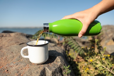 Photo of Woman pouring hot drink from thermos bottle into cup outdoors, closeup