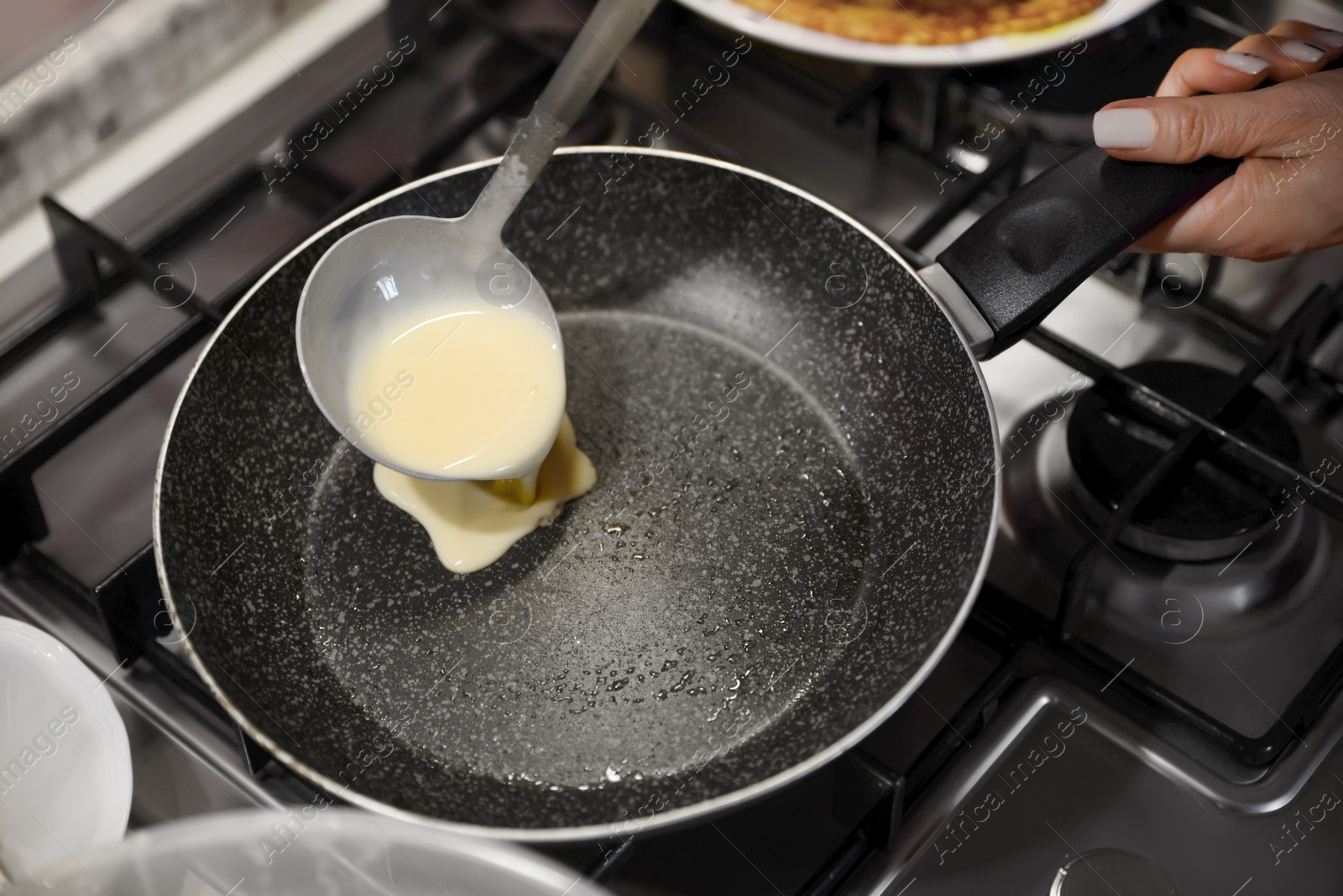 Photo of Woman pouring crepe batter onto frying pan in kitchen, closeup