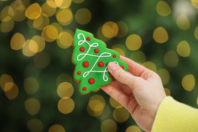 Photo of Woman with decorated cookie against blurred Christmas lights, closeup