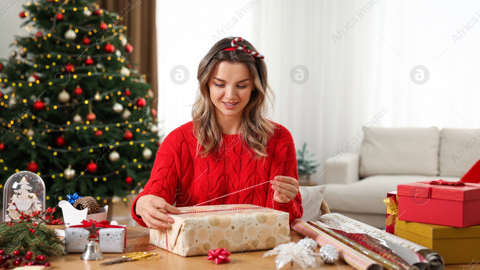 Photo of Beautiful young woman wrapping Christmas gift at home