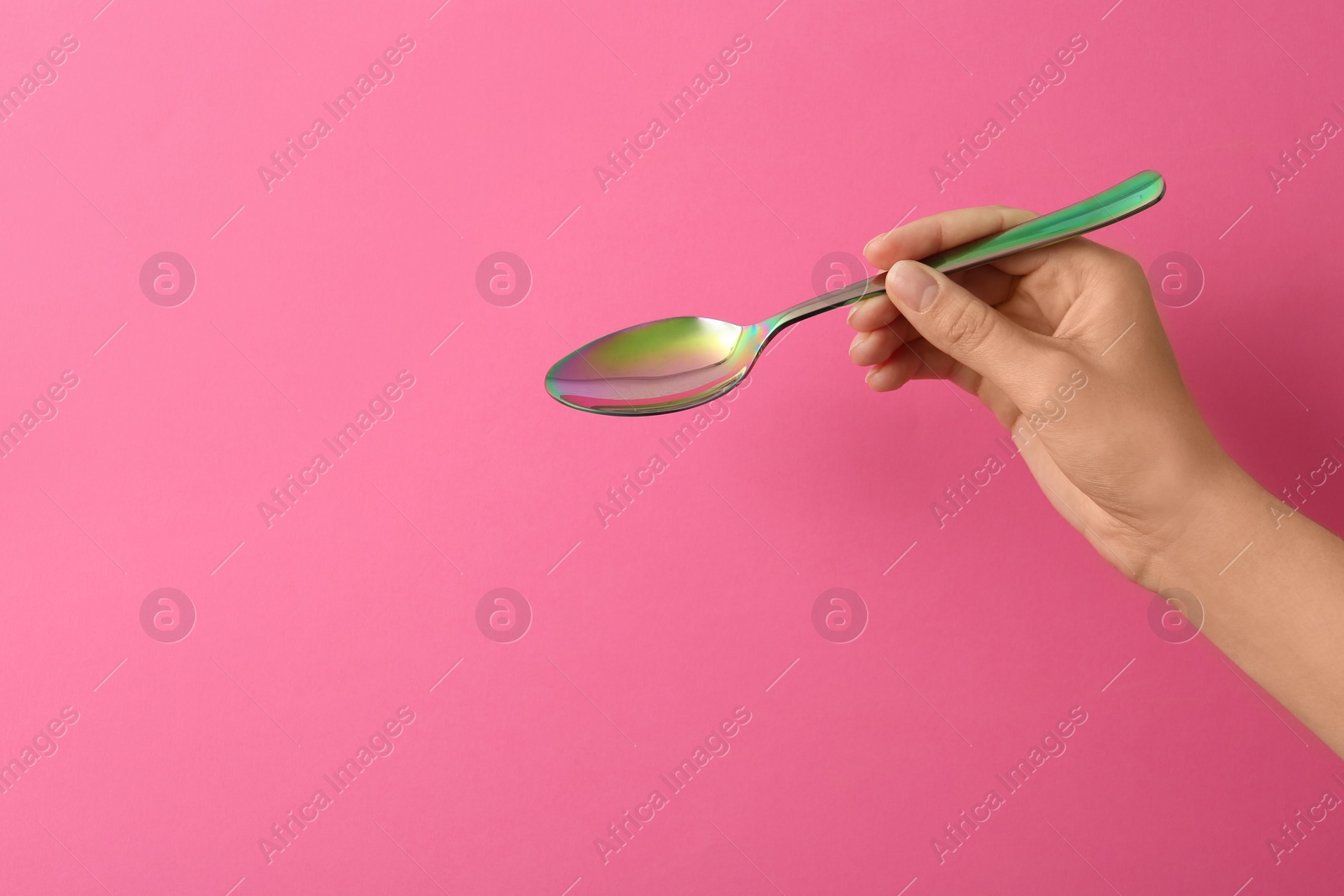 Photo of Woman holding empty table spoon on color background, closeup. Space for text