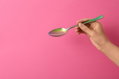 Woman holding empty table spoon on color background, closeup. Space for text