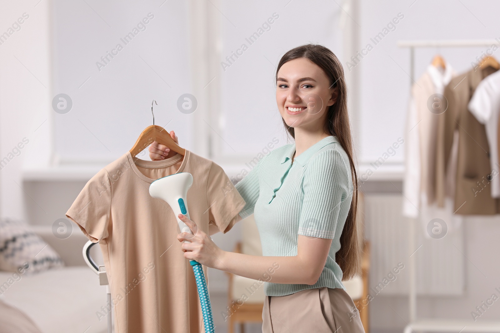 Photo of Woman steaming shirt on hanger at home