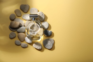 Bottle of luxury perfume in sunlight and stones on golden background, flat lay. Space for text