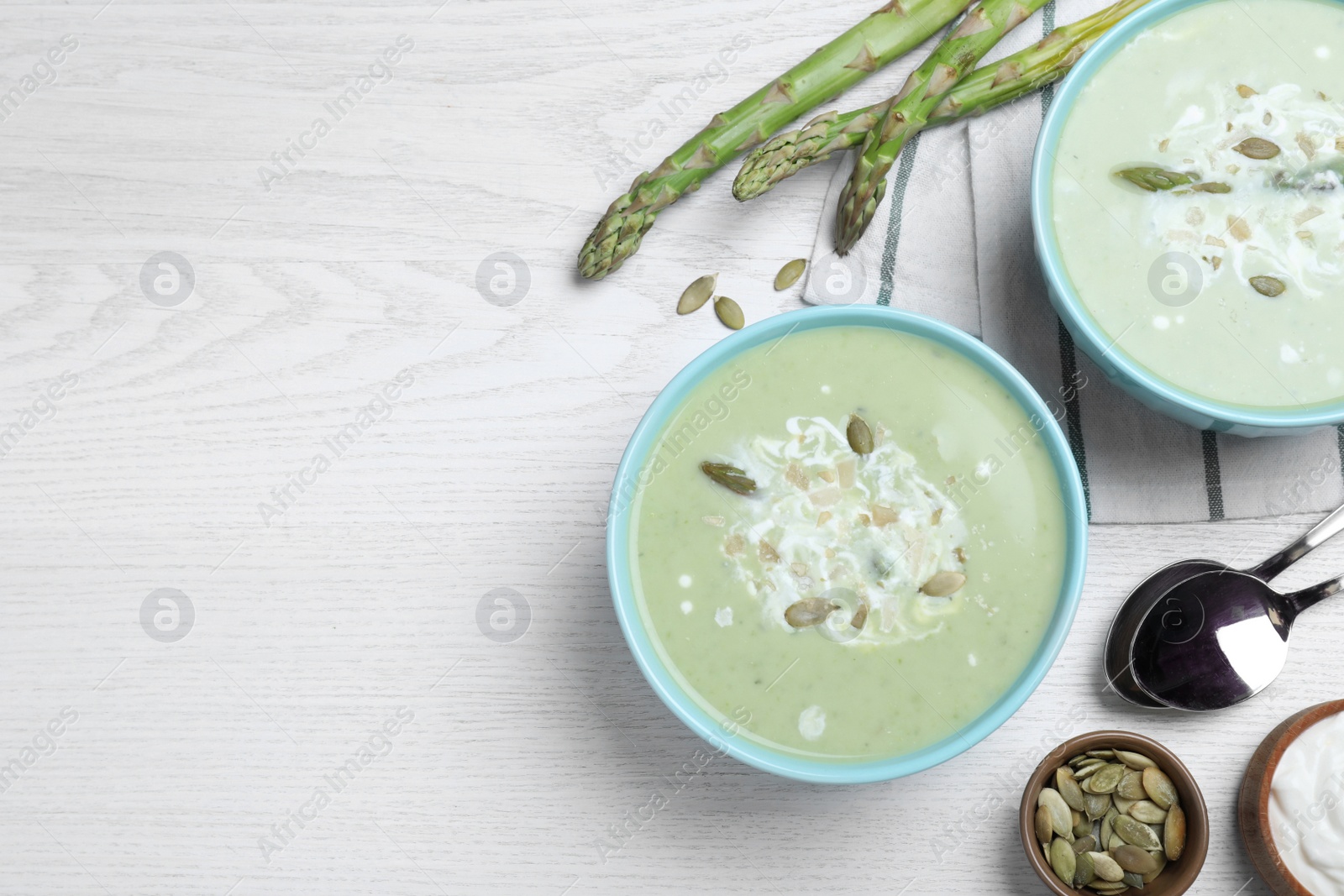 Photo of Bowls of delicious asparagus soup served on white wooden table, flat lay. Space for text