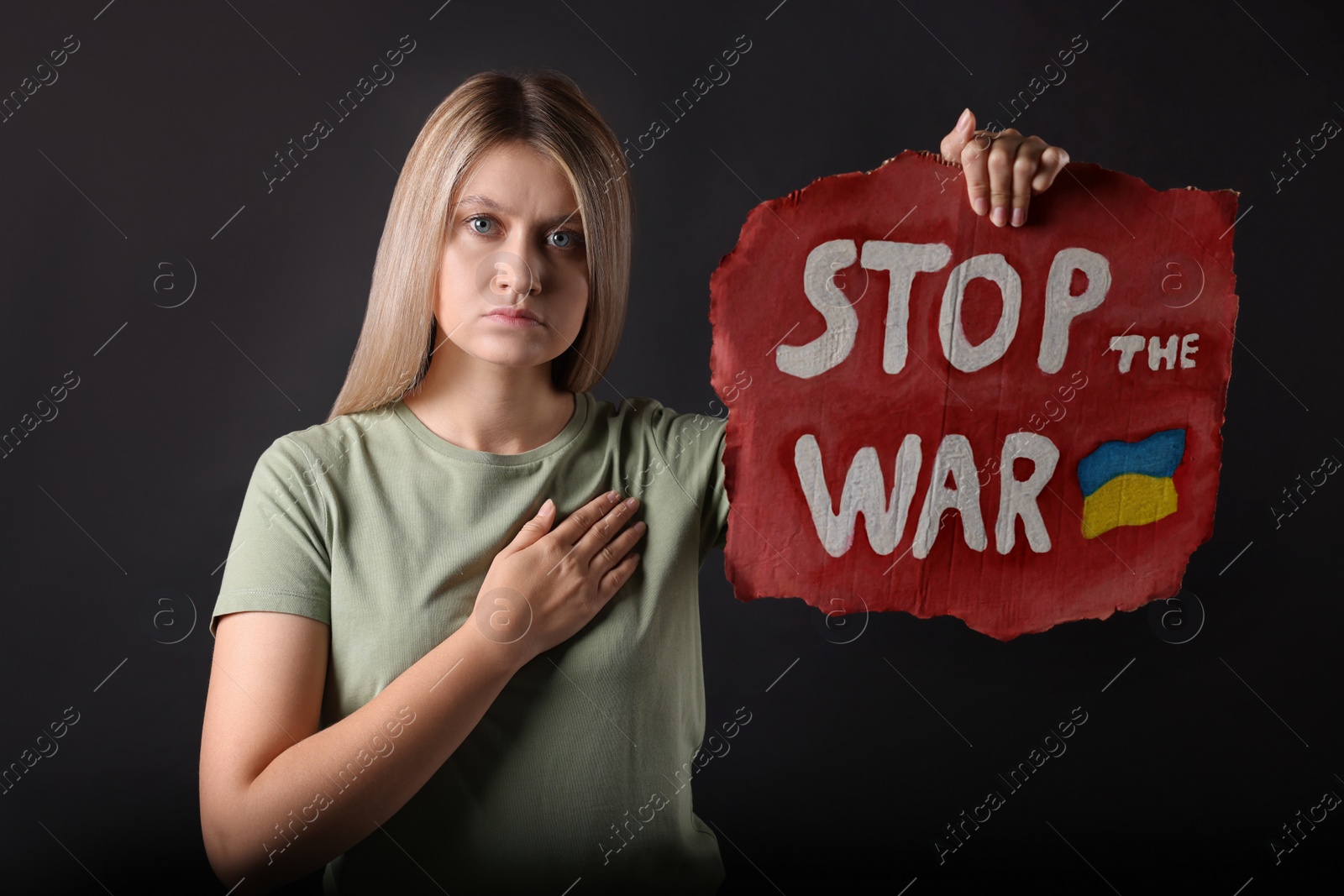 Photo of Sad woman holding poster with words Stop the War on black background