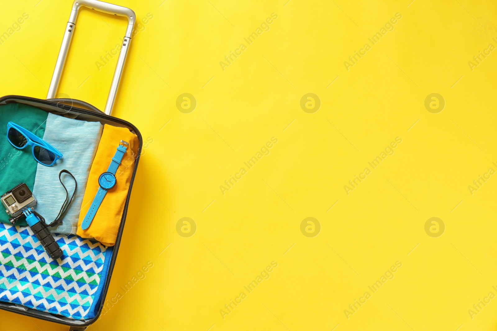 Photo of Open suitcase with summer clothes and accessories on color background, top view. Space for text