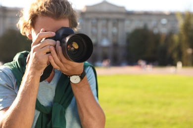 Young male photographer taking photo with professional camera on street. Space for text