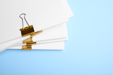 Photo of Many sheets of paper with golden clips on light blue background, top view. Space for text