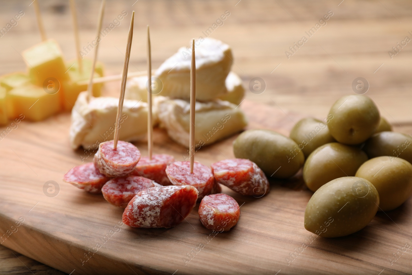 Photo of Toothpick appetizers. Pieces of sausage and olives on wooden table, closeup