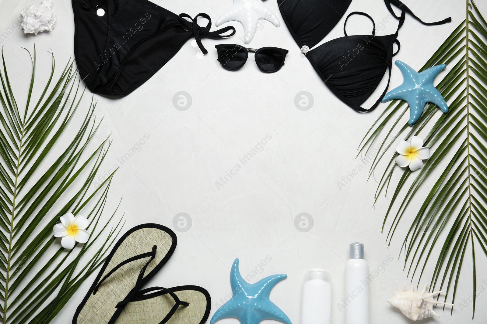 Photo of Frame made of black swimsuit and beach accessories on light stone background. Space for text