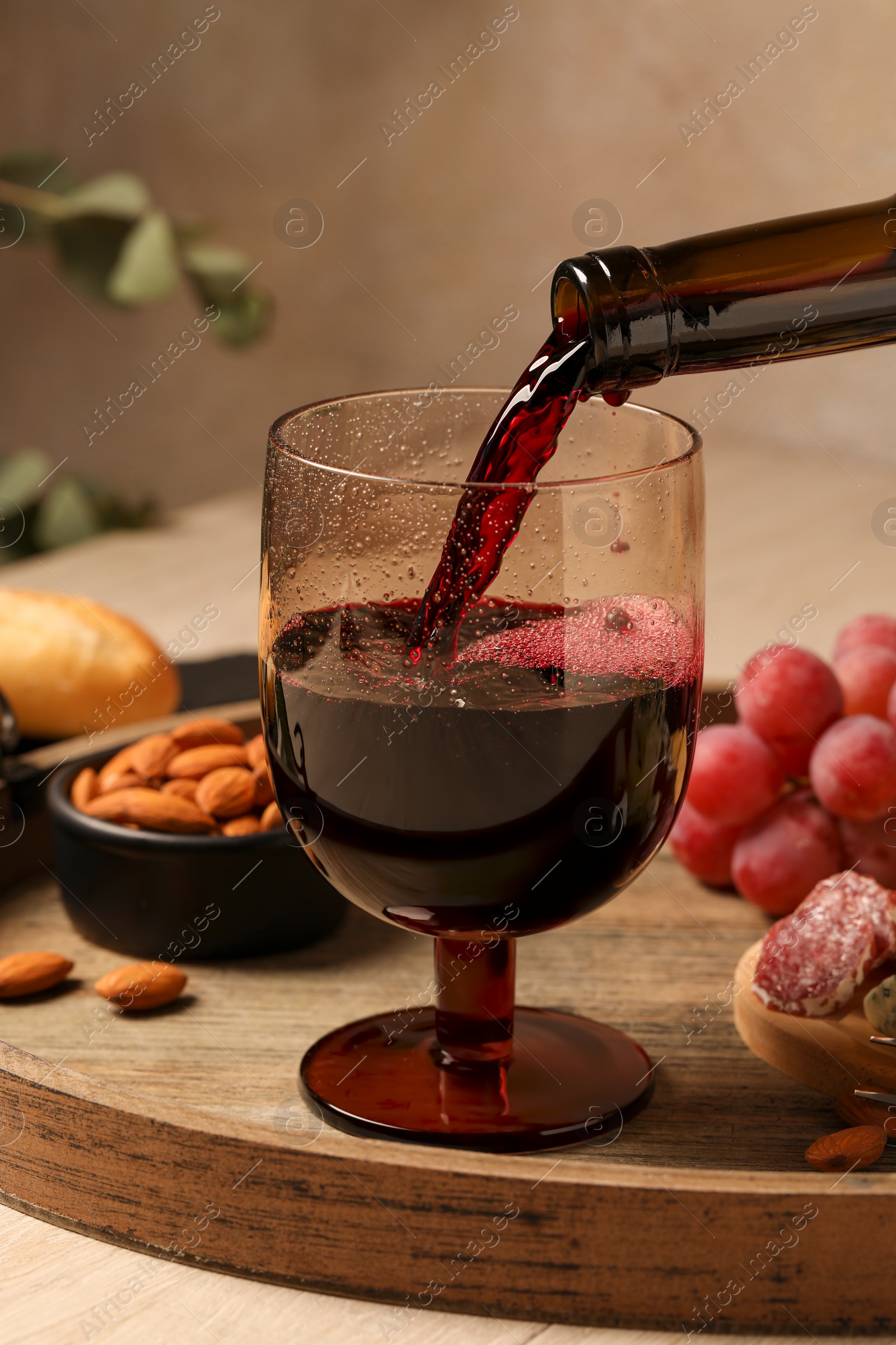 Photo of Pouring red wine into glass at wooden table, closeup