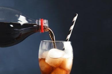 Photo of Pouring refreshing cola into glass with ice cubes on color background