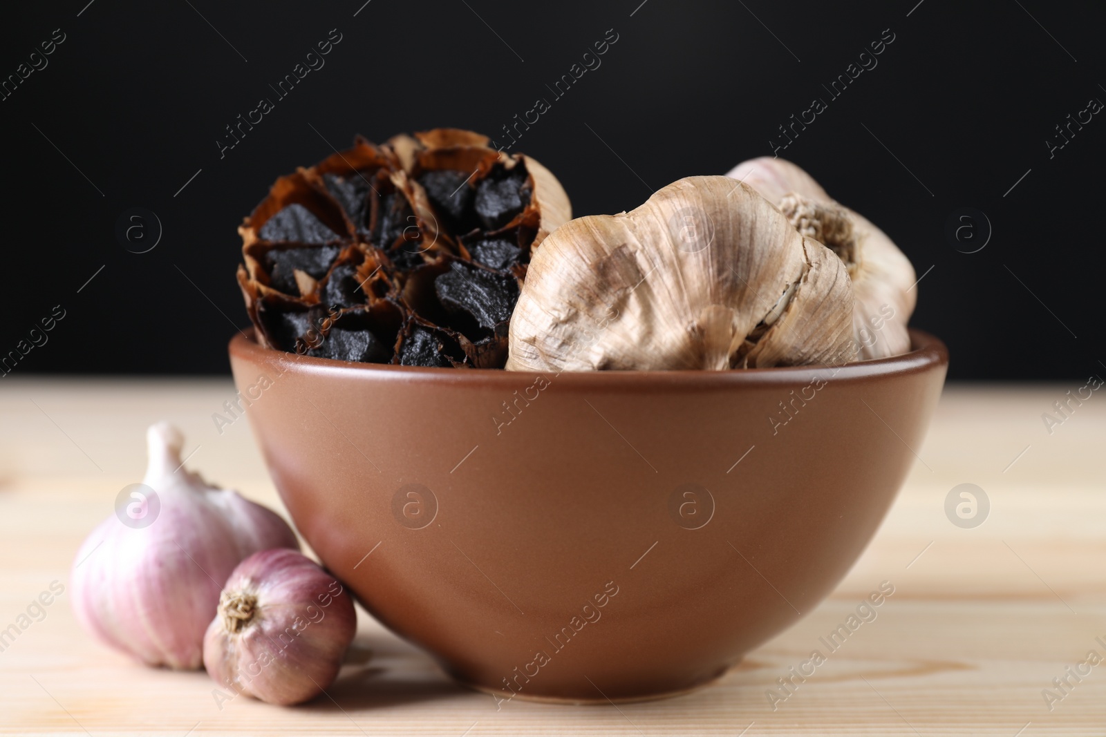 Photo of Bulbs of fresh and fermented black garlic on wooden table, closeup