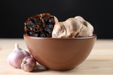 Photo of Bulbs of fresh and fermented black garlic on wooden table, closeup