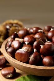 Photo of Fresh sweet edible chestnuts in wooden bowl on table, closeup