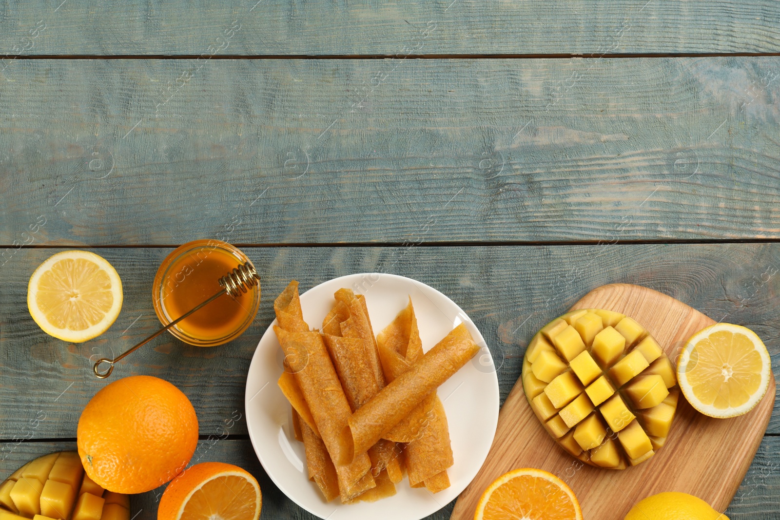 Photo of Flat lay composition with delicious fruit leather rolls on blue wooden table. Space for text