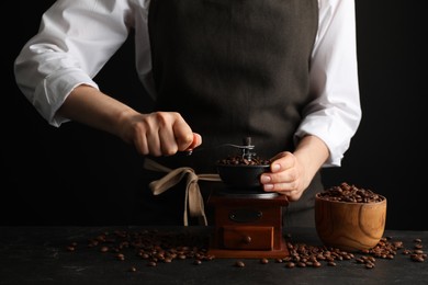 Photo of Woman using manual coffee grinder at black table, closeup