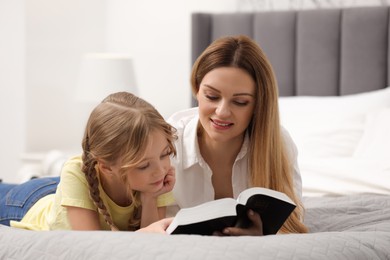 Girl and her godparent reading Bible together on bed at home