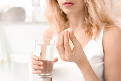 Young woman with pill and glass of water indoors