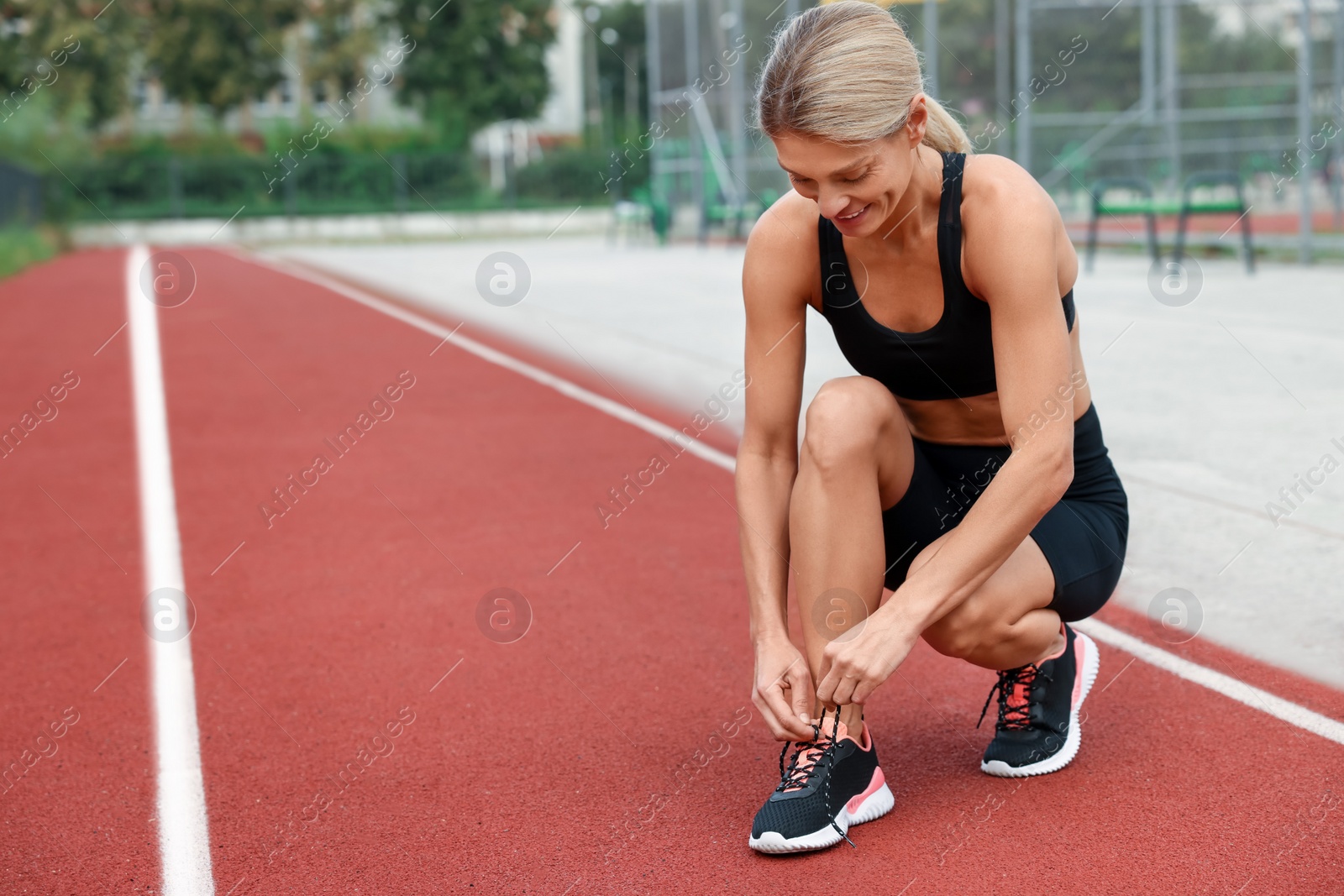 Photo of Happy woman tying shoelaces before training at outdoor gym, space for text