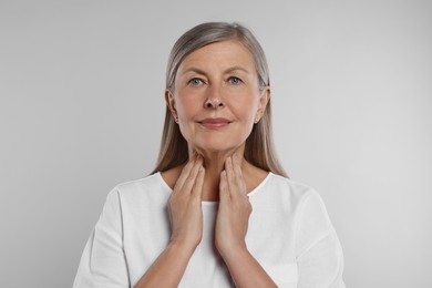 Endocrine system. Senior woman doing thyroid self examination on light grey background