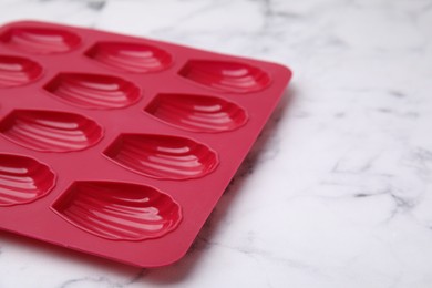 Photo of Red baking mold for madeleine cookies on white marble table, closeup. Space for text