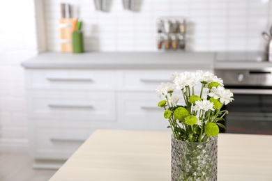 Vase with beautiful flowers on table in kitchen interior. Space for text