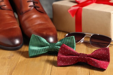 Stylish color bow ties, brown shoes and sunglasses on wooden background, closeup